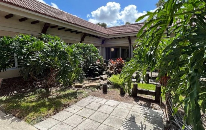 A serene courtyard garden with lush greenery and a stone pathway under a clear blue sky.