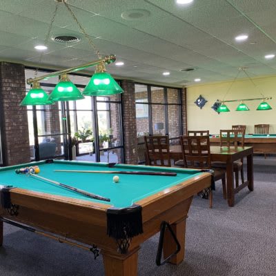 A recreation room featuring pool tables with green felt under bright overhead lights, alongside a seating area for players.