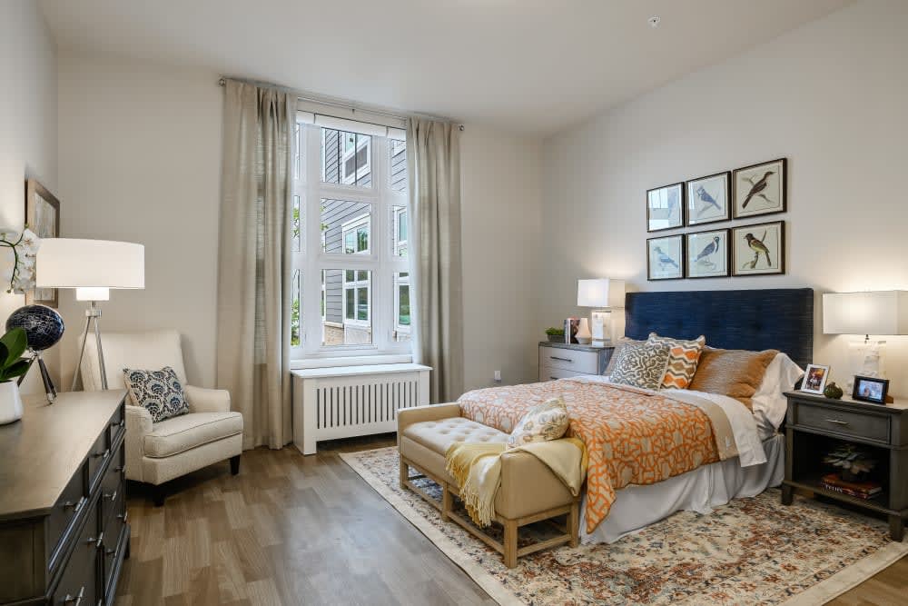 A modern, cozy bedroom with ample natural light, featuring elegant decor and a large window.