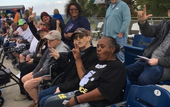 A group of people seated outdoors, some in wheelchairs, making peace signs.