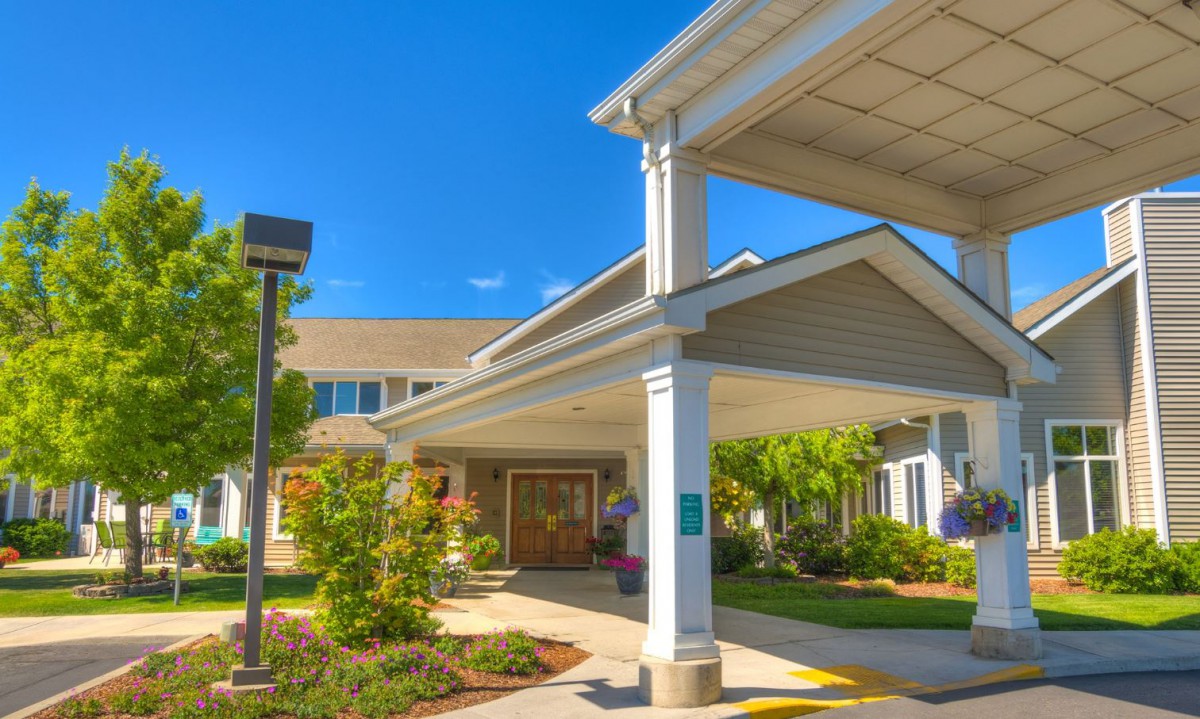 A sunny day view of a building entrance with a white canopy and landscaped surroundings.