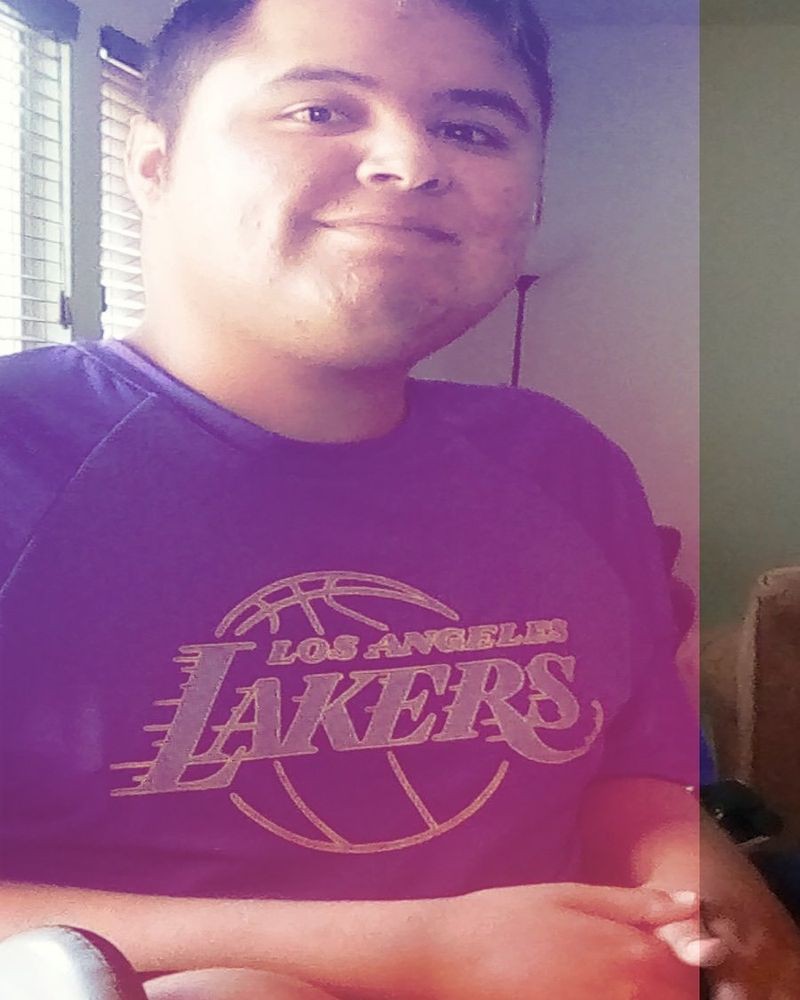 A person smiling, wearing a Los Angeles Lakers T-shirt indoors.