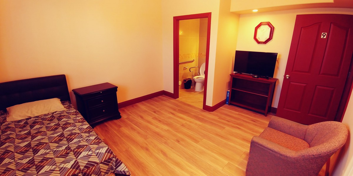 A cozy bedroom with wooden flooring, featuring a television and an open doorway leading to a bathroom.