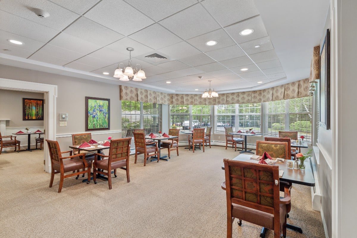 A well-lit dining area with multiple tables and chairs, featuring large windows and pleasant decor.