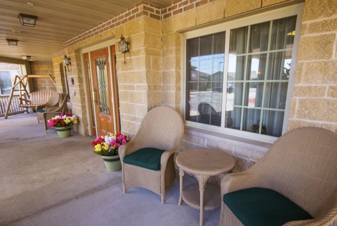 A cozy porch area with two chairs, a small table, and colorful flowers by the front door.