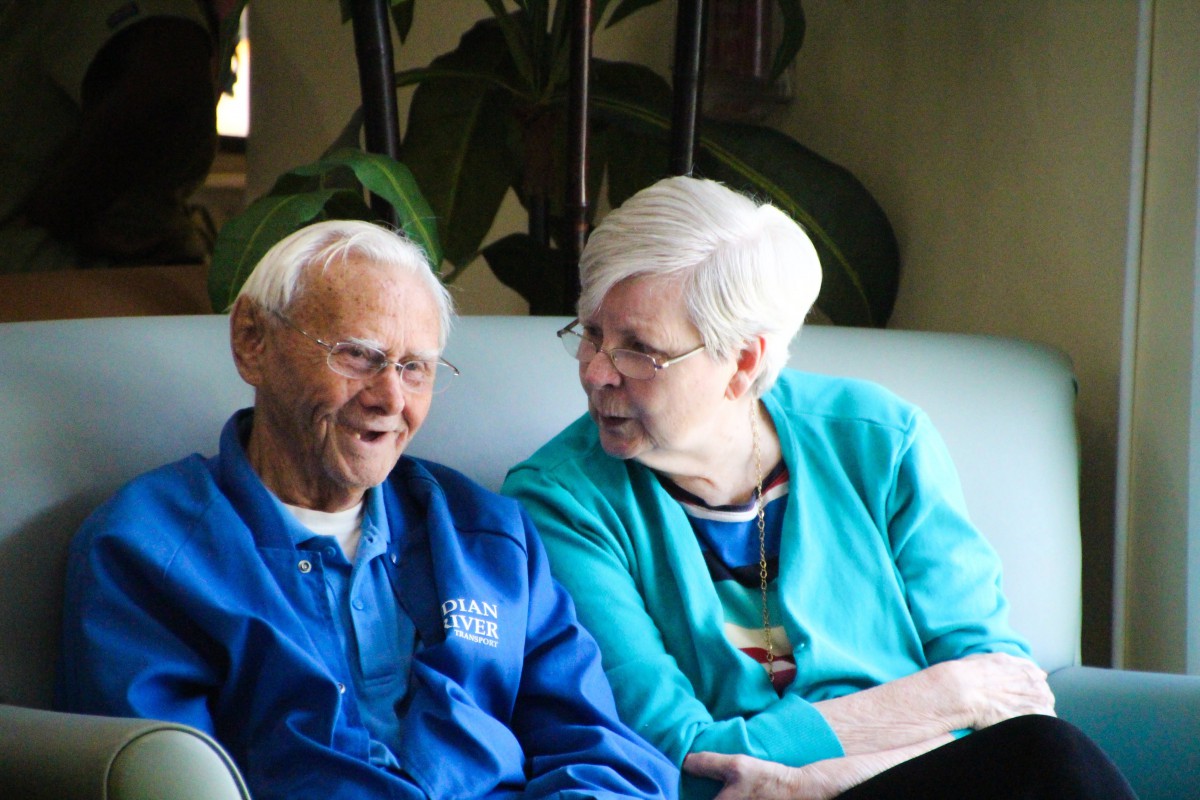 An elderly couple enjoys a cheerful conversation while sitting indoors.
