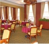 A restaurant dining area with multiple tables and chairs arranged near large windows with curtains.
