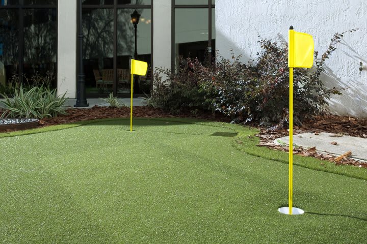 A small outdoor putting green with yellow flags on artificial turf.