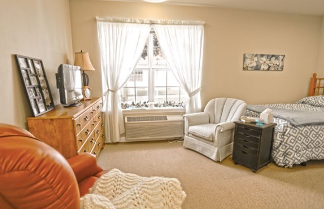 A cozy living room with an armchair, television, and a large window with curtains.
