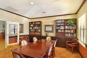 A cozy library or meeting room with bookshelves and a wooden table surrounded by chairs.