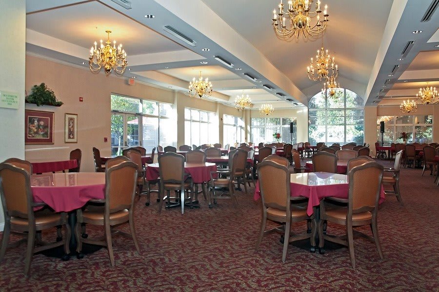 A spacious dining room with elegant chandeliers, arranged tables and chairs, and large windows allowing natural light.