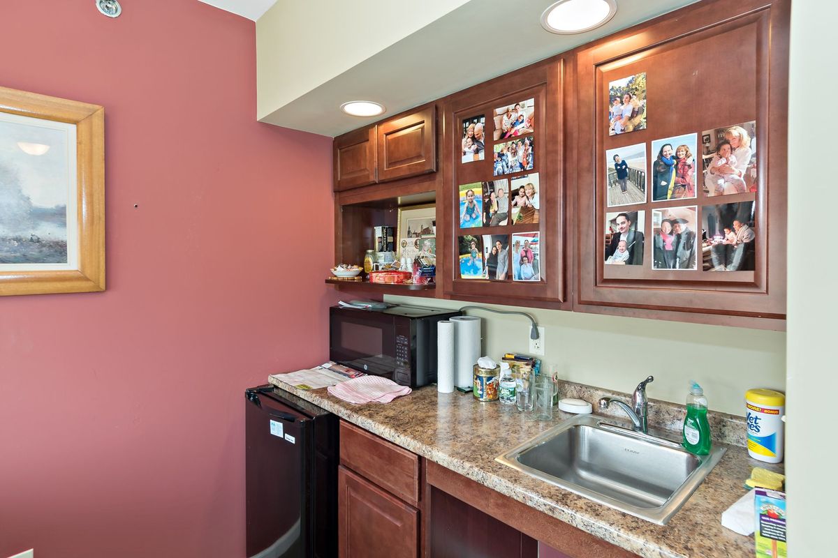 A cozy kitchenette with a mini-fridge, microwave, and countertop adorned with personal photos on the cabinet doors.