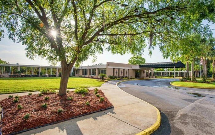 A sunny view of a building entrance surrounded by trees and landscaped grounds.