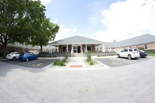 A well-maintained building with a clear blue sky, surrounded by greenery and parked cars.