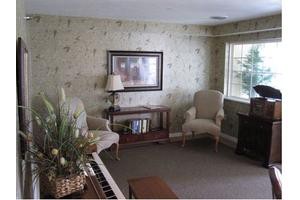 A cozy living room with a piano, armchairs, and a bookshelf near a large window.
