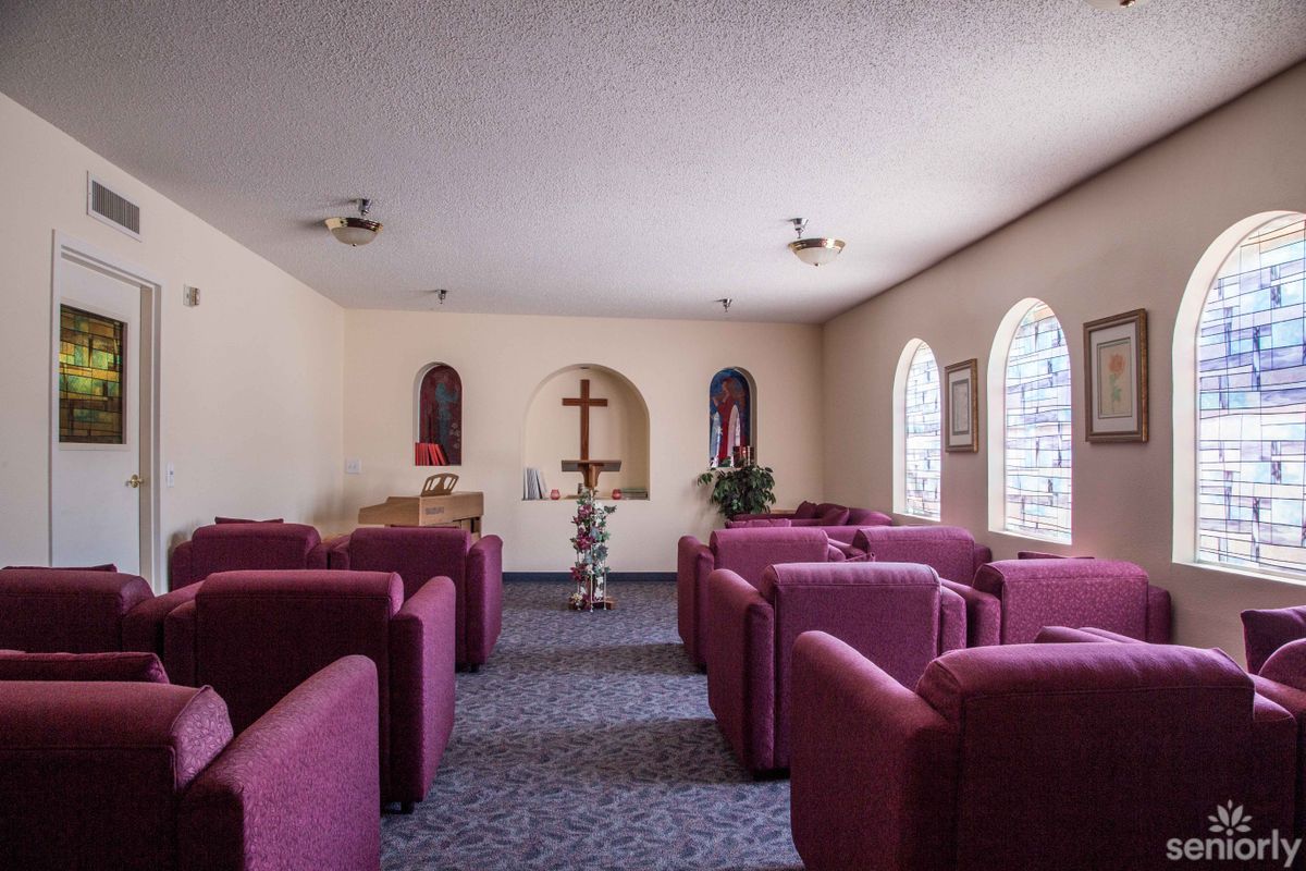 A small chapel with rows of upholstered seating facing a cross on the wall.