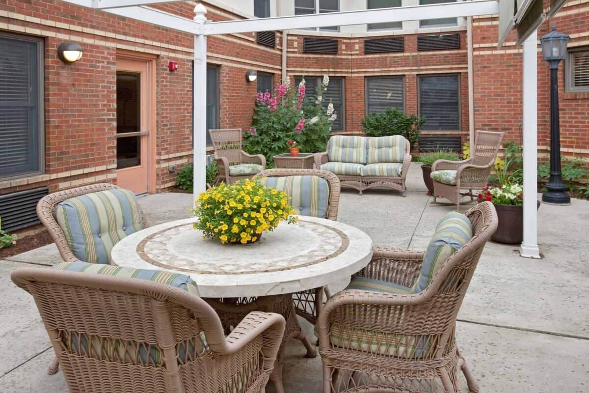 A cozy patio area with wicker chairs and a table adorned with flowers in a brick courtyard.