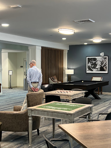 A man stands in a modern lounge area featuring a pool table and comfortable seating.