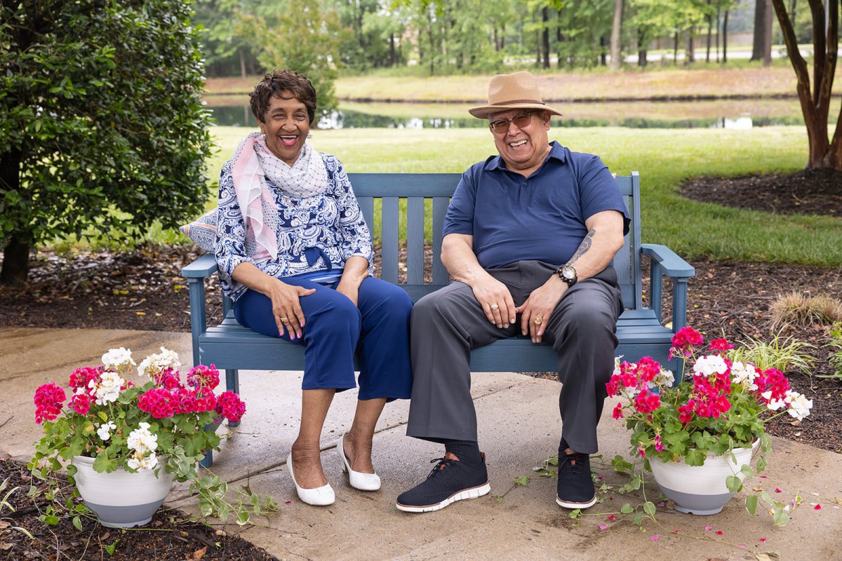 A couple sitting on a bench surrounded by flowers in a park.