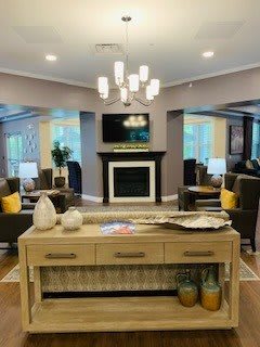 A modern living room with a stylish chandelier, comfortable seating, and a fireplace beneath a wall-mounted TV.