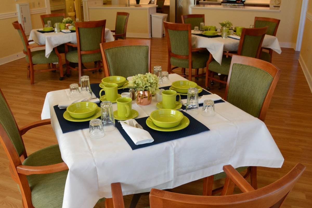 A neatly set dining table with green dishes and a floral centerpiece in a restaurant setting.