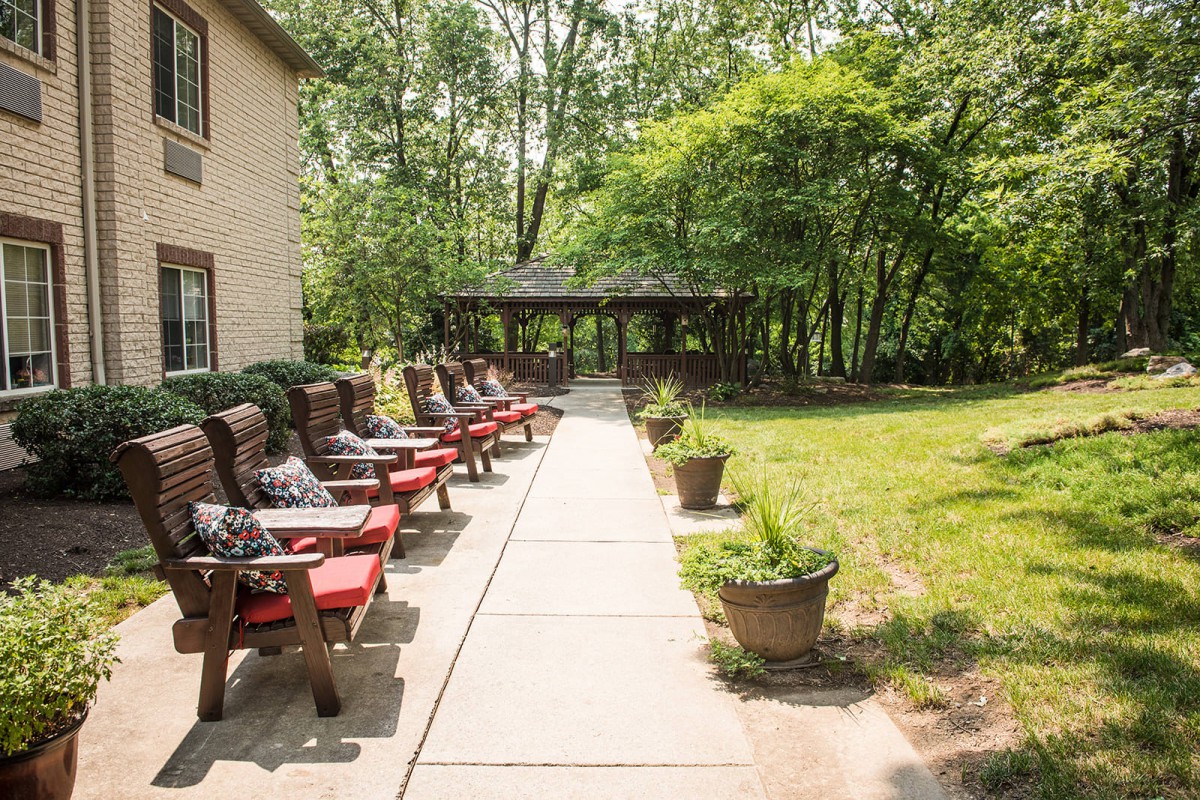 A peaceful outdoor patio area with rows of chairs and a pathway leading to a gazebo surrounded by lush greenery.