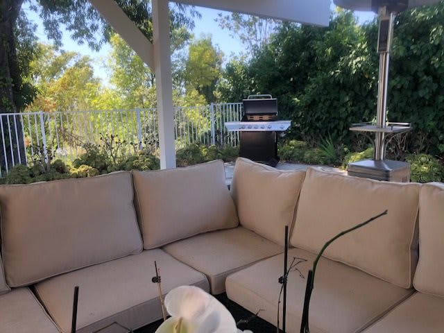 A cozy outdoor patio with comfortable seating and a grill in the background.
