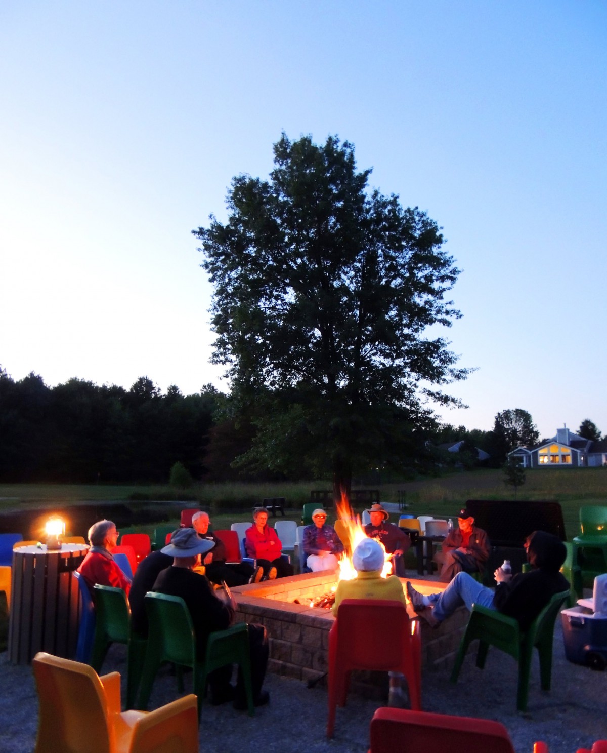 A group of people gathered around a campfire in an outdoor setting during the evening.