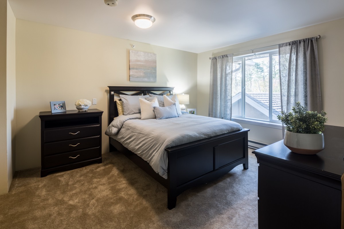 A cozy bedroom with a large bed, dresser, and natural light from a window.