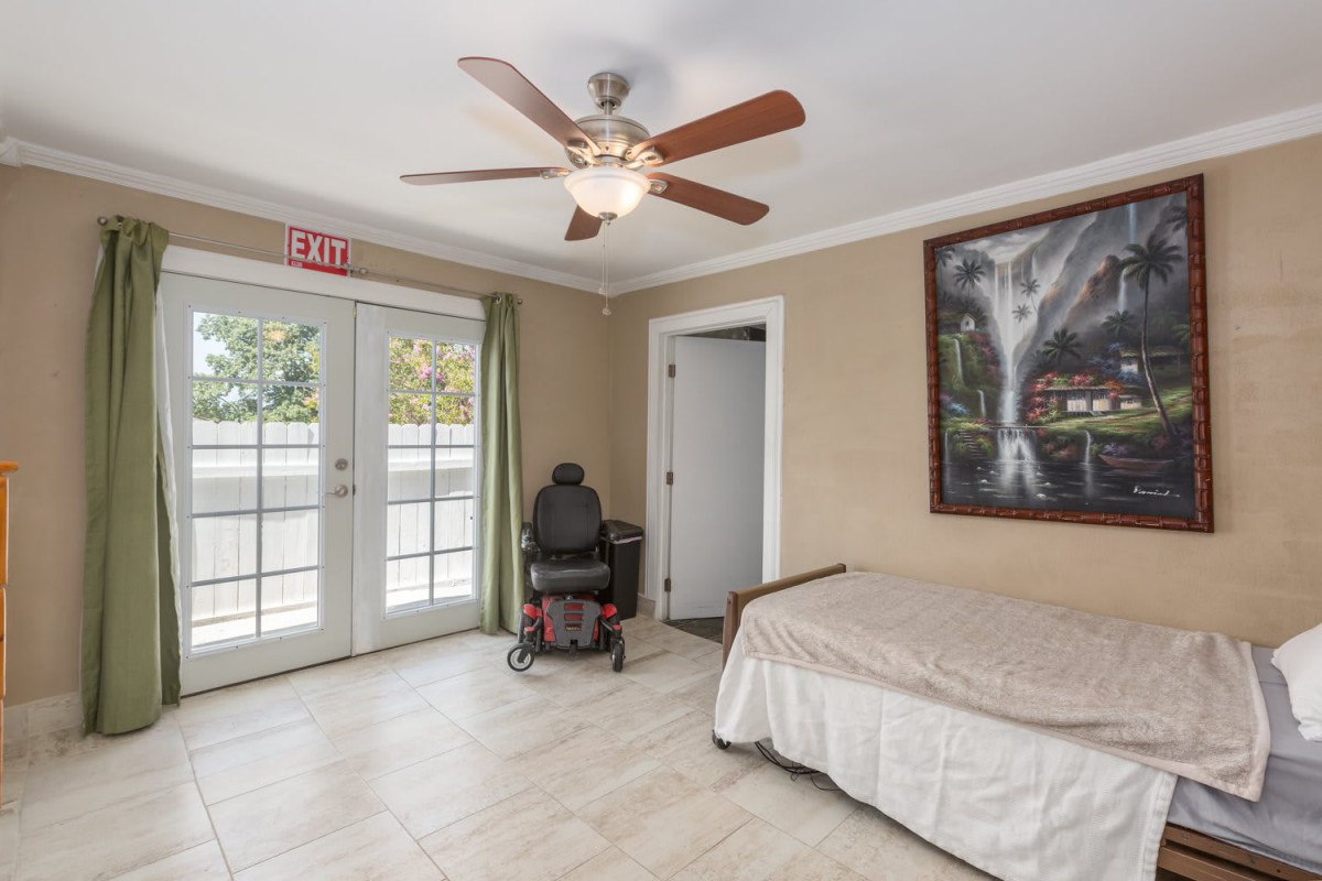 A room with a bed, ceiling fan, and wheelchair next to French doors.