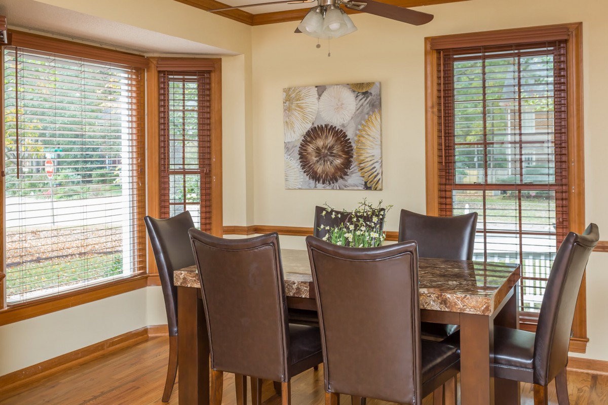 A cozy dining room featuring a wooden table with six leather chairs, surrounded by large windows and decorated with wall art.