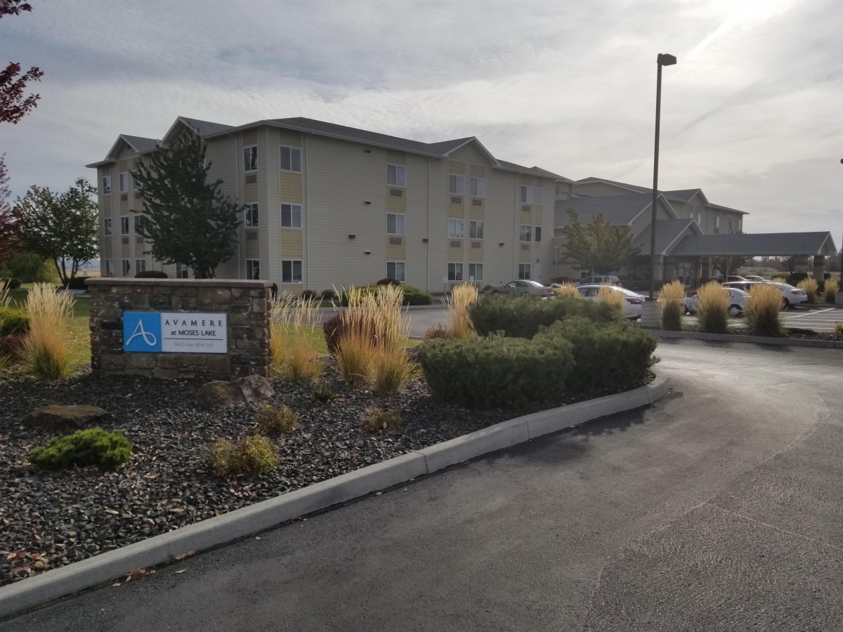 A residential apartment complex with well-maintained landscaping and a parking area on an overcast day.