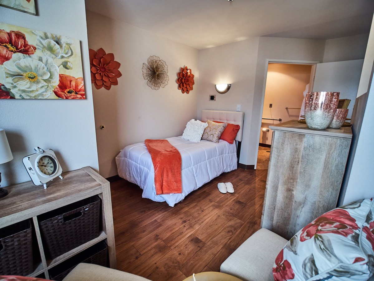A cozy bedroom with orange accents and a single bed, featuring wooden flooring and stylish decor.