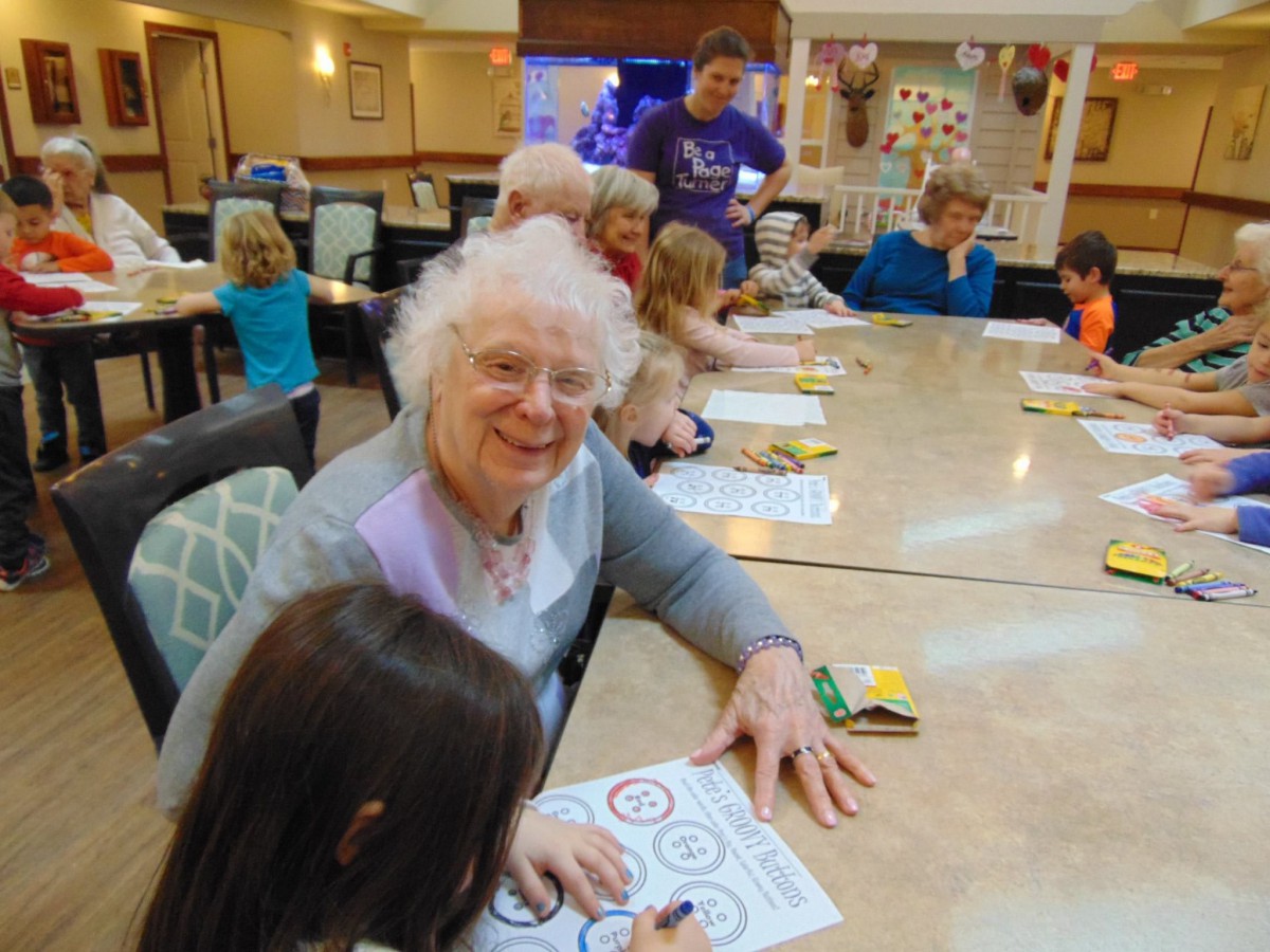A group of elderly people and children engage in a collaborative art activity at a community center.