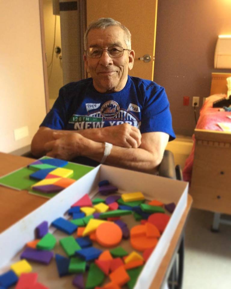 An elderly person smiling while sitting at a table with colorful puzzle pieces.