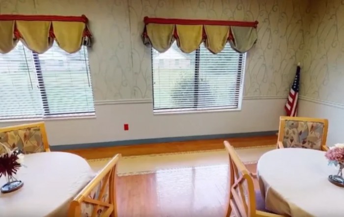 A dining area featuring tables, chairs, and windows with decorative curtains.