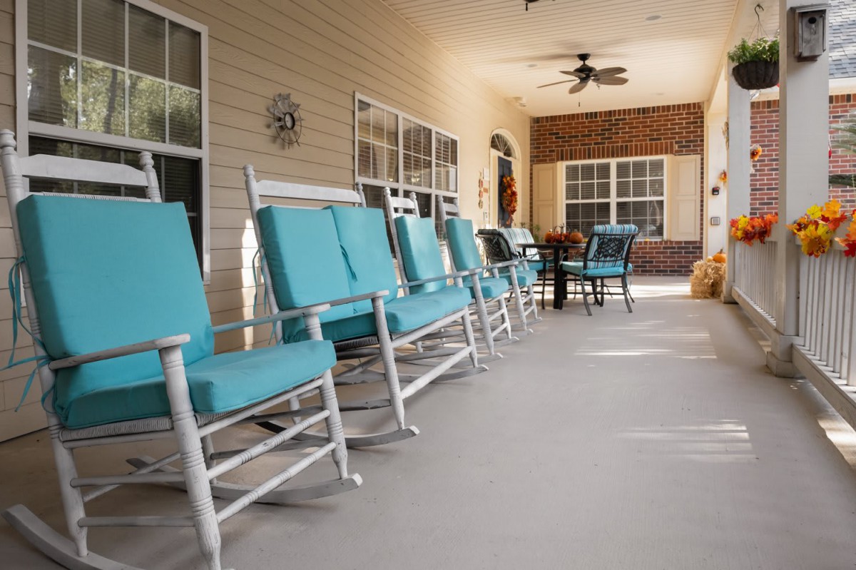 A cozy porch with a row of blue-cushioned rocking chairs and a ceiling fan.