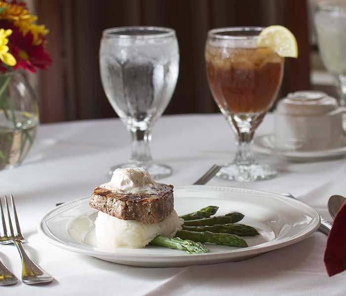 A beautifully plated steak served with mashed potatoes and asparagus, accompanied by a glass of water and iced tea in an elegant restaurant setting.