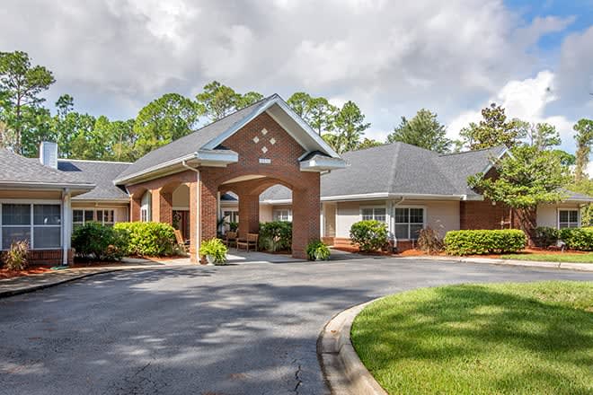 A welcoming entrance to a residential building with a landscaped driveway and surrounding trees.