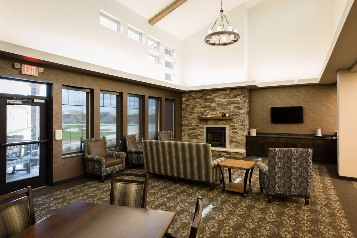 A modern living room with comfortable seating around a stone fireplace, featuring large windows and contemporary lighting.