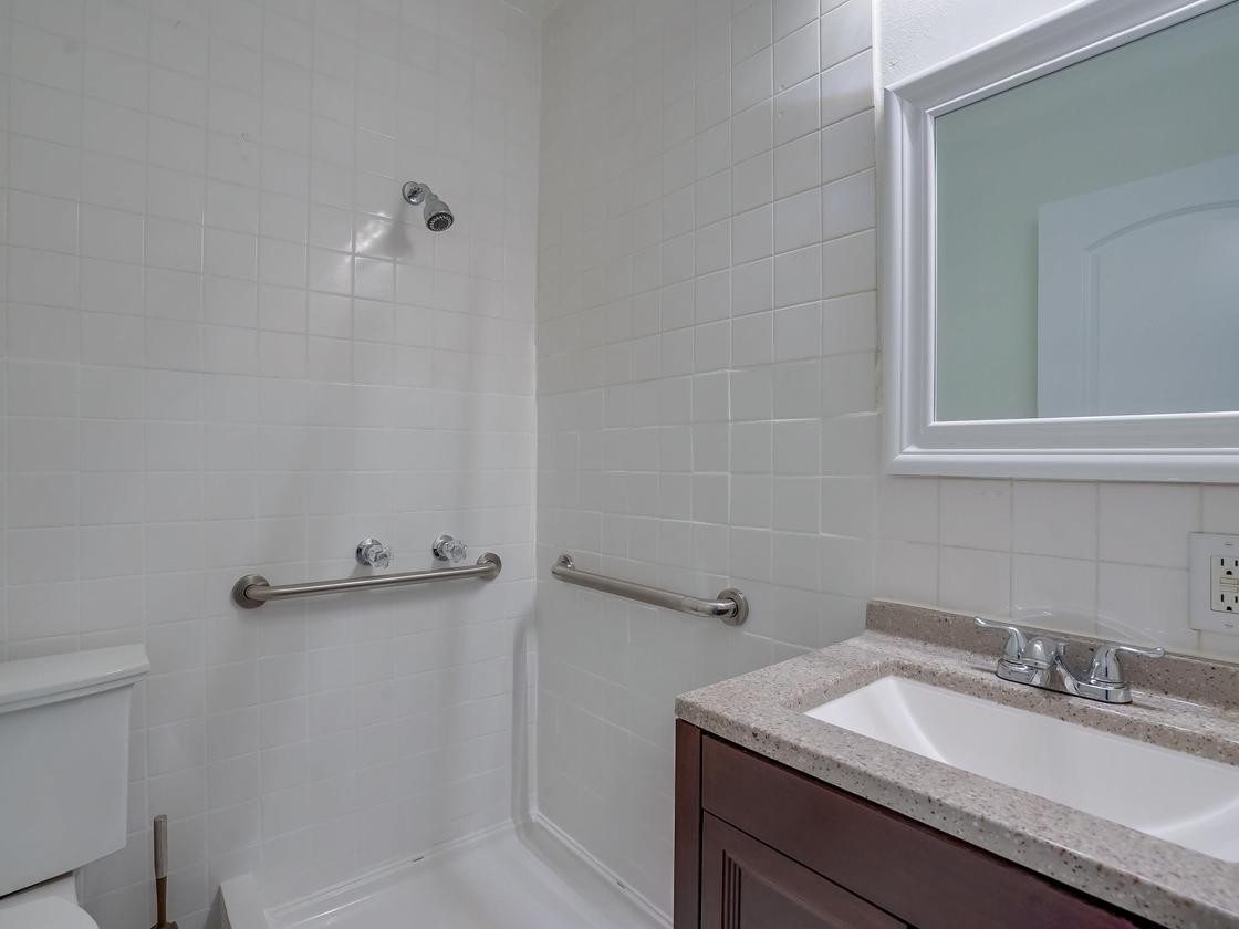 A bathroom with a walk-in shower, featuring grab bars for safety and a sink on the right side.