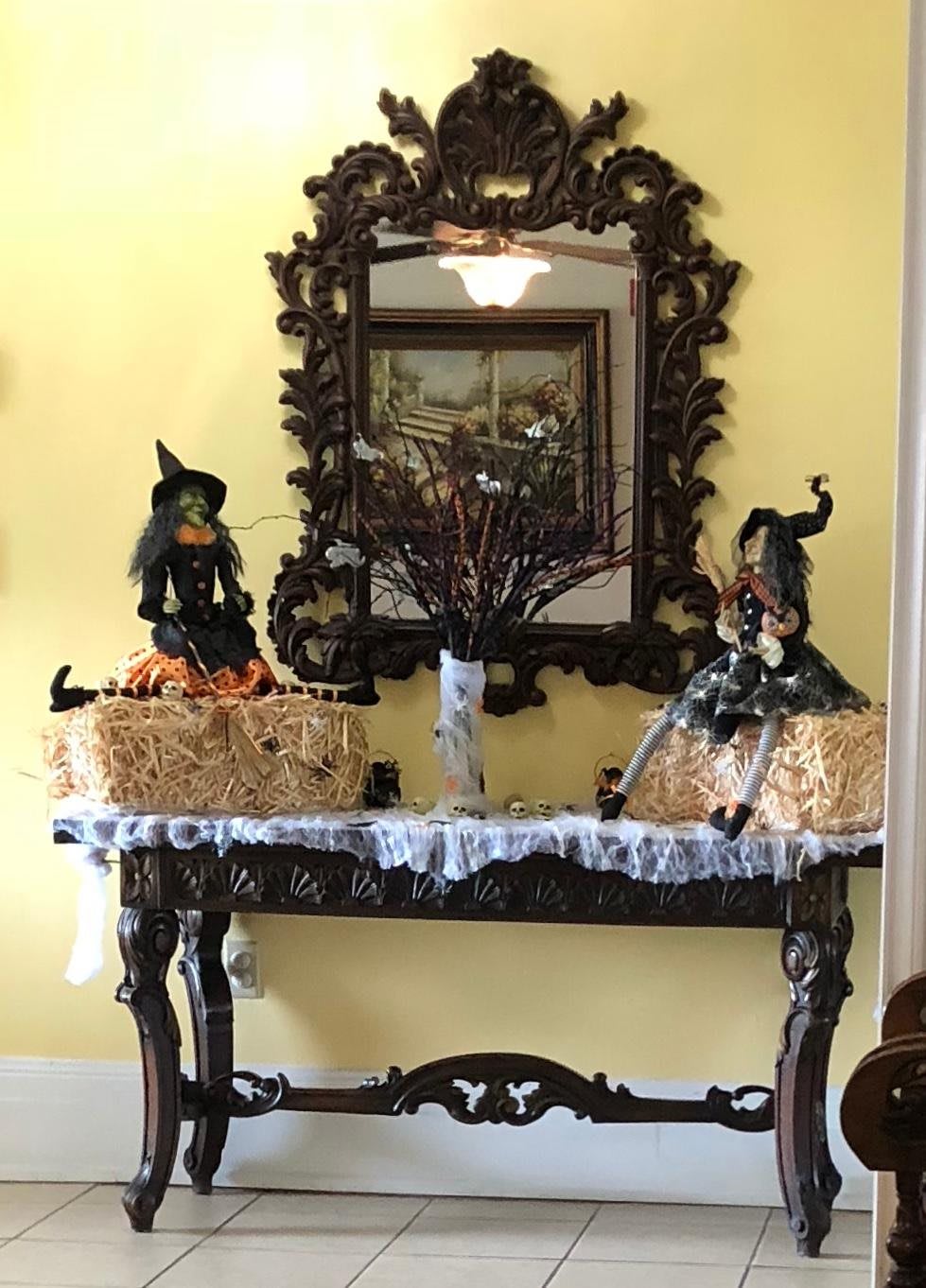 A cozy indoor setup featuring Halloween decorations, including witch figurines on a table with a mirror backdrop.