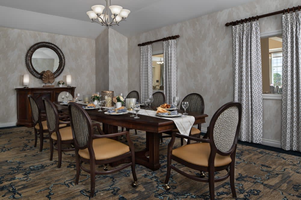 A spacious dining room with a classic wooden table set for dinner, surrounded by elegant chairs and adorned with a chandelier.