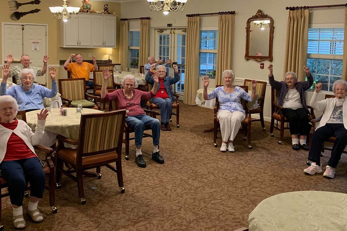 A group of seniors participating in a seated exercise activity in a community room.