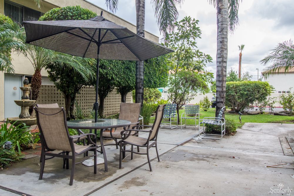 A tranquil patio setting with a table, chairs, and an umbrella surrounded by lush greenery.