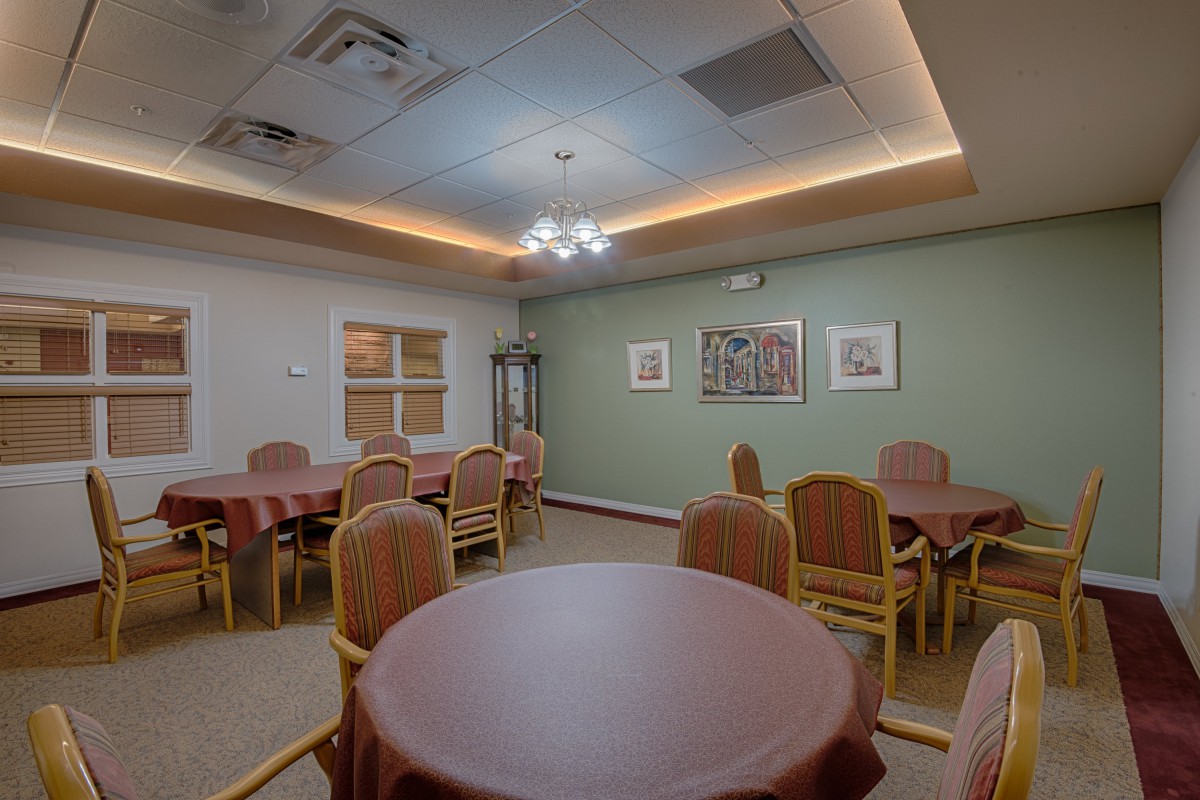 A cozy dining room with several round tables and chairs, warmly lit with ceiling lights.
