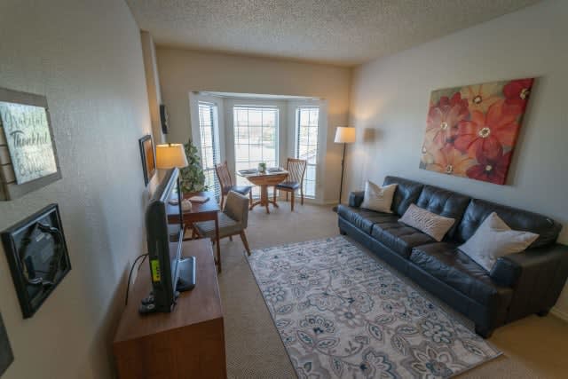 A cozy living room with a sofa, TV, and a dining set near large windows.