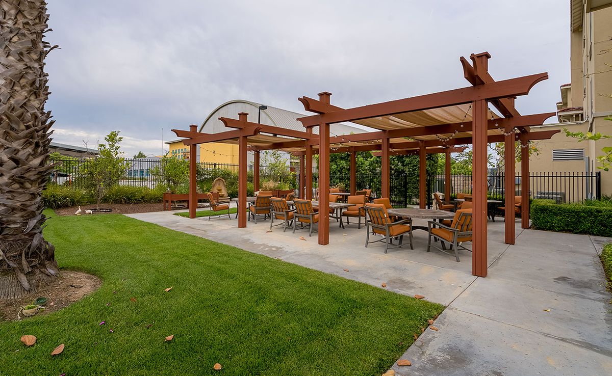 An outdoor seating area with a wooden pergola and patio furniture, set in a landscaped garden.