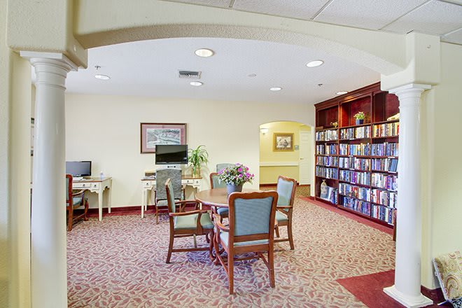 A cozy library reading area with bookshelves, a table and chairs, and a computer station.