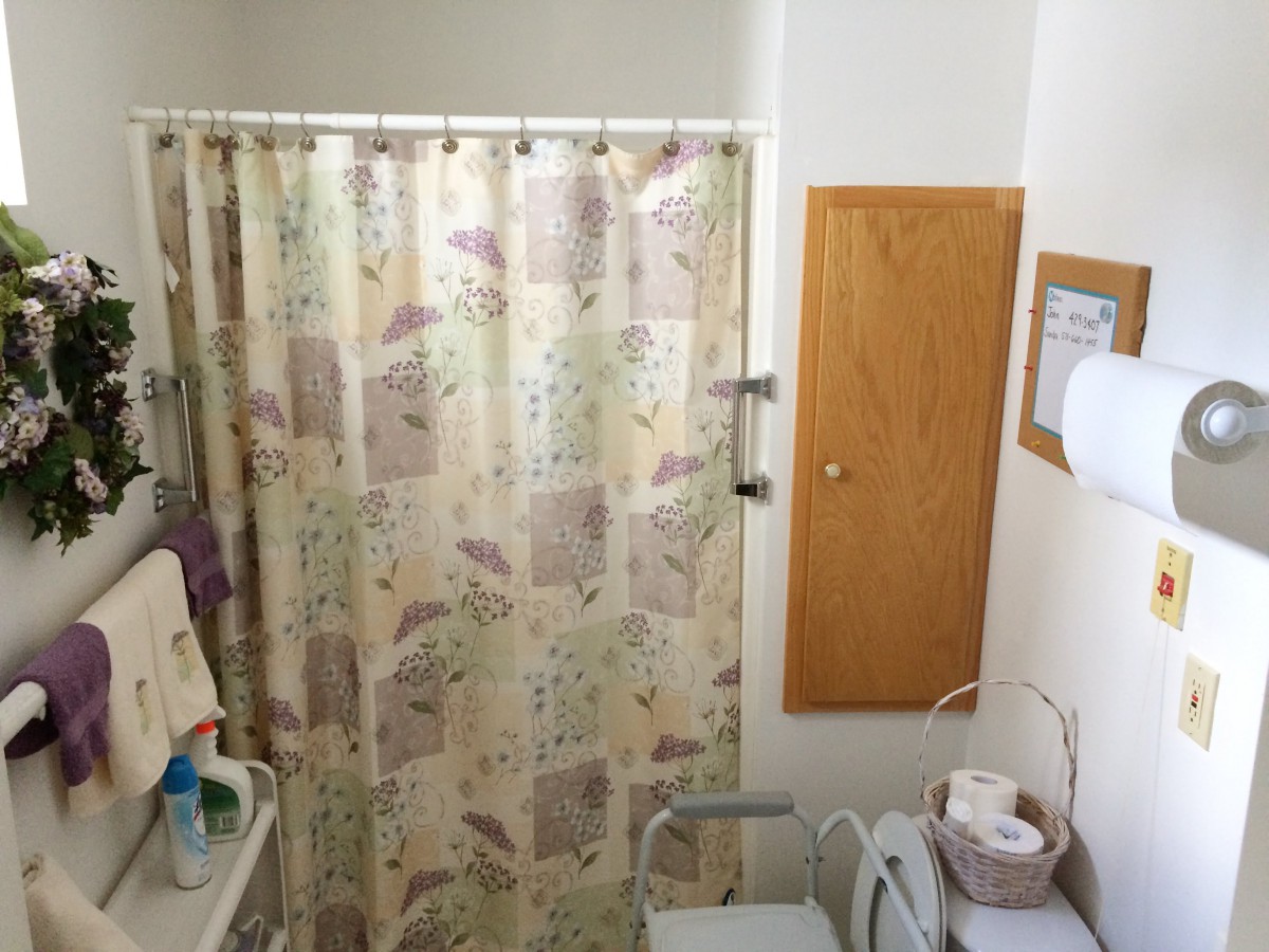 A small bathroom with a floral shower curtain, wall cabinet, and various toiletries.